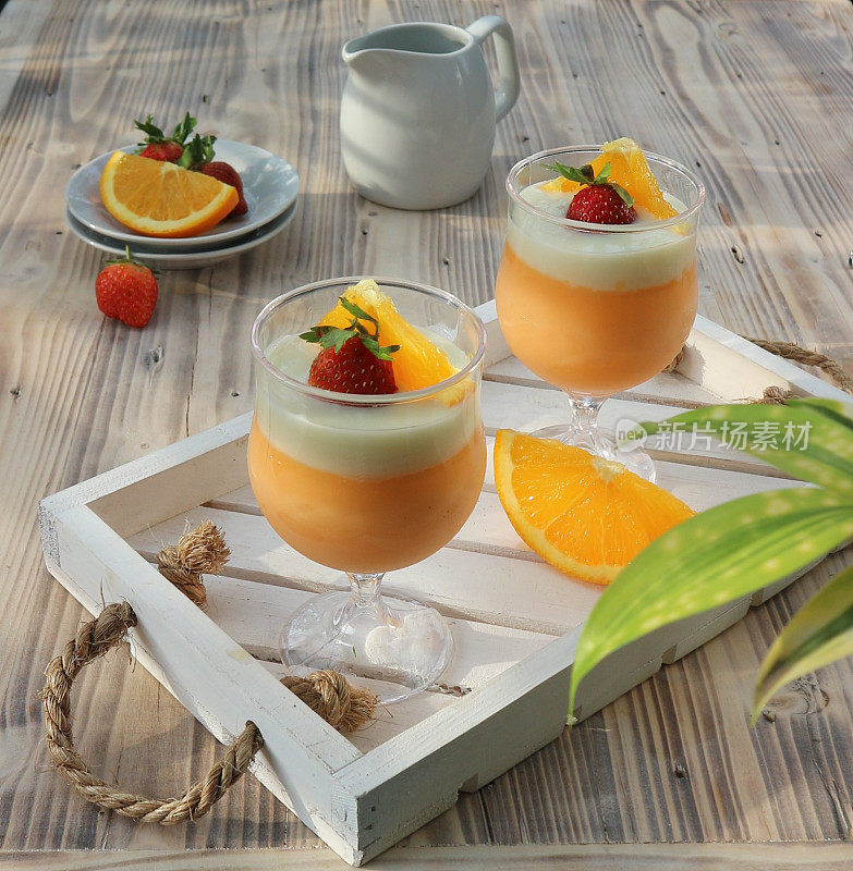 two orange puddings in glasses garnished with sliced ​​oranges and strawberries served on a wooden tray
